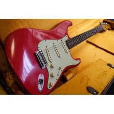 a red electric guitar sitting on top of a wooden table next to an open case