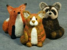 three small stuffed animals sitting next to each other on a gray surface and one is red, the other brown