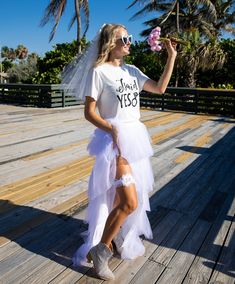 a woman in a white wedding dress holding a pink flower while standing on a wooden deck