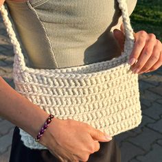 a woman is holding a crocheted bag in one hand and a beaded bracelet on the other