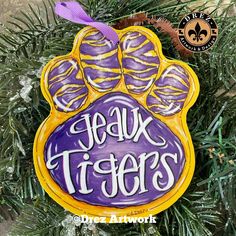 a purple and yellow ornament hanging from a christmas tree with the words faux tigers painted on it