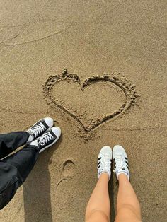 two people are standing in the sand with their feet in the sand and one is drawing a heart