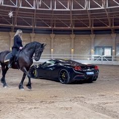 a woman riding on the back of a horse next to a black car in an arena