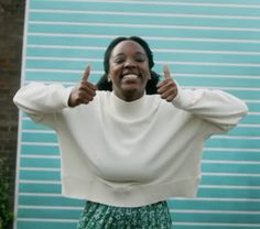 a woman with her hands on her hips giving the thumbs up in front of a blue wall