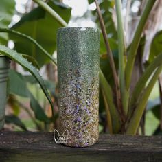 a green vase sitting on top of a wooden table next to a potted plant