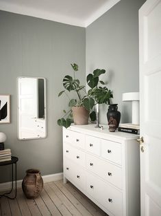 a white dresser sitting next to a mirror on top of a wooden floor in a room