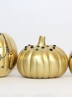 three gold painted pumpkins sitting next to each other on a white surface with black dots