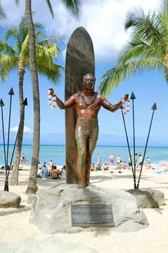 a statue of a man holding a surfboard in front of palm trees on the beach