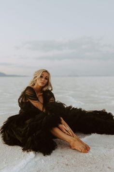 a woman sitting on the beach in a black dress