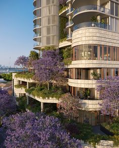 the building has many balconies and plants growing on it's sides, along with purple trees