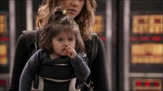 a woman holding a small child in her back pack while standing next to an airport sign