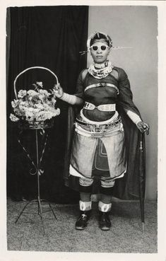 an old black and white photo of a man in costume holding a basket with flowers on it