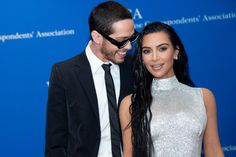 a man and woman standing next to each other in front of a blue wall wearing sunglasses