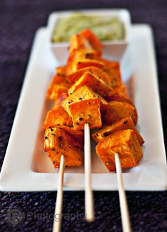 skewers of tofu on a white plate with dipping sauce in the background