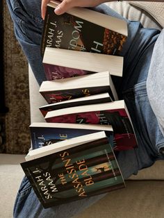 a person is sitting on a couch with many books in their lap and holding one