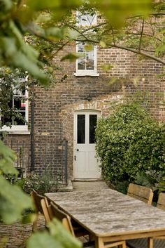 a wooden table and chairs in front of a brick building with a white door on it