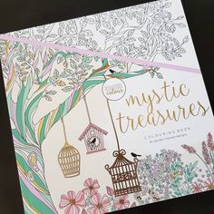 an adult coloring book with flowers and birdcages on the cover, in front of a black background