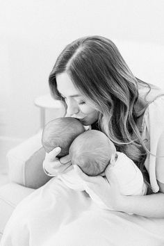 a woman holding a baby in her arms while laying on a bed with white sheets