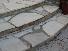 the steps are made of stone and have potted plants on each side, along with brick pavers