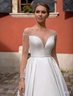 a woman in a white wedding dress standing on a cobblestone street with her hands in her pockets