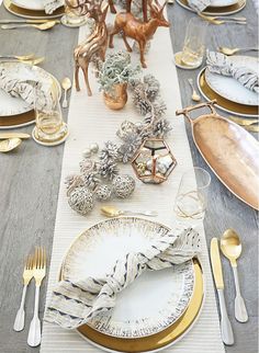 the table is set with gold and white plates, silverware, and deer figurines