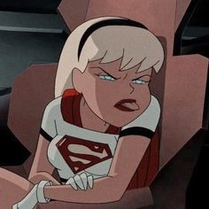 a woman with blonde hair and blue eyes wearing a superman t - shirt sitting down