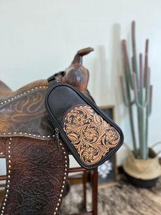 a brown and black horse saddle sitting on top of a wooden table next to a cactus