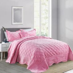 a bed with pink bedspread and pillows in a white room next to a window