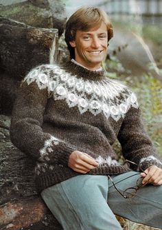 a man sitting on top of a tree trunk wearing a sweater