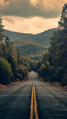 an empty road with trees and mountains in the background