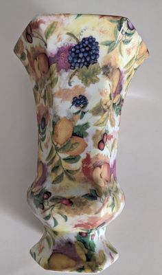 a vase with fruit and flowers painted on it's sides, sitting against a white background