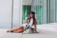 a woman in graduation attire sitting on the ground with her husky dog wearing a hat