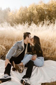 a man and woman sitting on top of a blanket kissing in the middle of a field