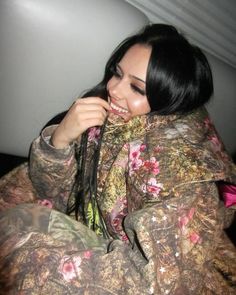 a woman wrapped up in a blanket smiling and looking at the camera while sitting down