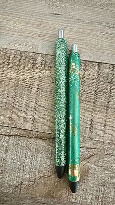 two green pens sitting on top of a wooden table next to each other with gold flakes all over them