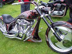 a motorcycle parked on top of a lush green field next to other motorcycles and people