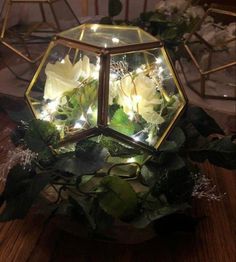 a glass vase filled with white flowers on top of a wooden table covered in greenery