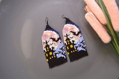 two pairs of beaded earrings sitting on top of a plate next to a plant