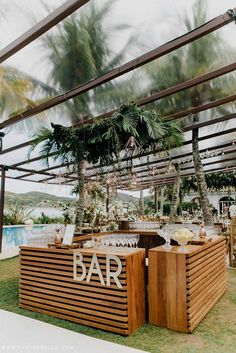 an outdoor bar is set up with palm trees and greenery in the background for a tropical wedding reception