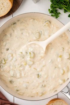 a large pot filled with white sauce next to bread and parsley on the side