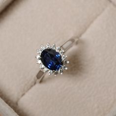 a ring with a blue stone surrounded by small white diamonds in a velvet presentation box