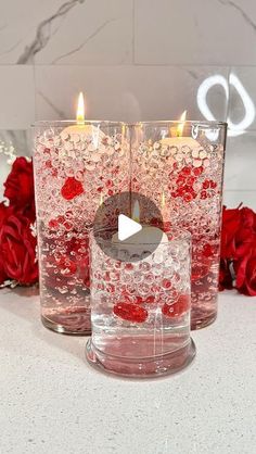 two clear glass vases with candles in them on a table next to red roses