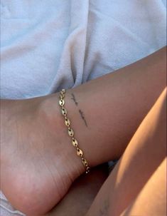 a close up of a person's foot with a gold chain bracelet on it