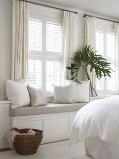 a white bed sitting next to a window covered in pillows and blankets on top of a wooden bench