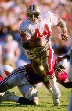 a football player running with the ball in his hand and another person on the ground behind him