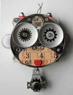 a clock with gears and numbers on it's face hanging from a hook in a wall