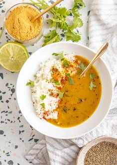 a white bowl filled with rice, curry and cilantro on top of a table