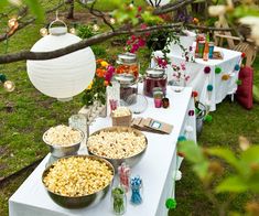 a table topped with lots of food on top of a lush green field next to a tree