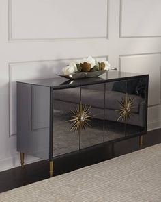 a mirrored cabinet with gold starburst decorations on the top and bottom, in front of a white wall