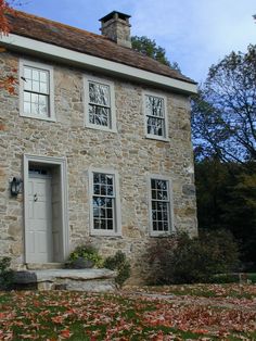 an old stone house with two windows and a clock on the front door is surrounded by fall leaves